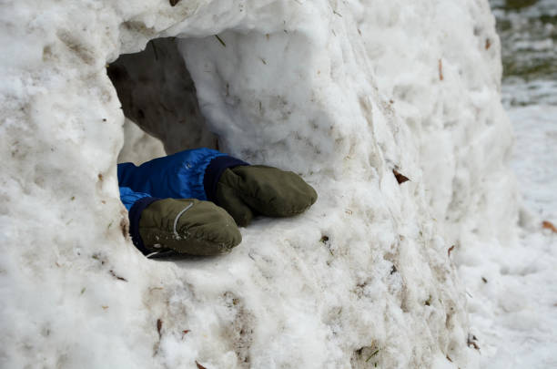 małe dziecko w zimie coveralls spacery zbuduje igloo. mały chłopiec wystaje ręce z jaskini lodowej, dziury, domu. ma rękawiczki z palców i próbuje wydostać się z zamarzniętego otworu - blizzard house storm snow zdjęcia i obrazy z banku zdjęć