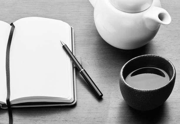 drinking tea and writing on a copy book Open copybook with blank page on a wooden desk; close-up with teapot and cup filled with hot drink. Pen. sobriety stock pictures, royalty-free photos & images