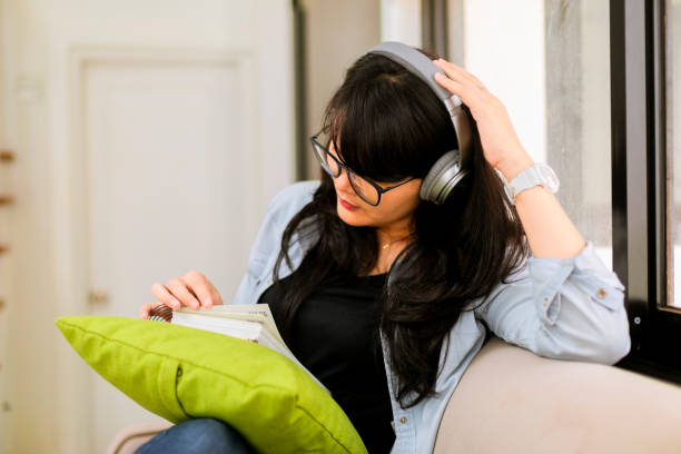 istock asian young woman sitting on couch at home reading a book 1297032413