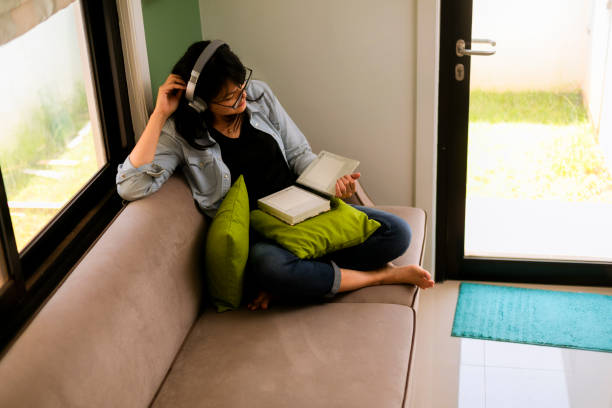 istock asian young woman sitting on couch at home reading a book 1297032577