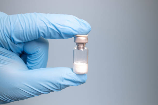 Doctor drawing up Covid-19 vaccine from glass phial bottle and filling syringe injection for vaccination. Close up of hand wearing protective disposable gloves in lab and holding a bottle of vaccination drugs. Hand with blue surgical gloves taking sars-coV-2 vaccine dose from vial with syringe: prevention and immunization concept.