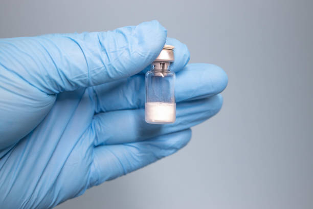 Doctor drawing up Covid-19 vaccine from glass phial bottle and filling syringe injection for vaccination. Close up of hand wearing protective disposable gloves in lab and holding a bottle of vaccination drugs. Hand with blue surgical gloves taking sars-coV-2 vaccine dose from vial with syringe: prevention and immunization concept.