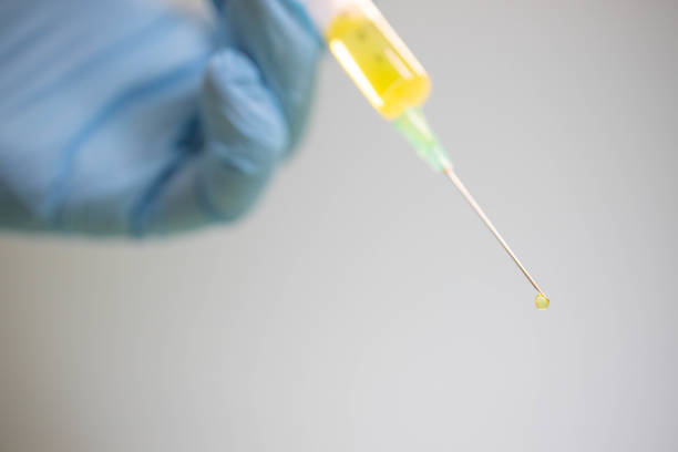 Doctor drawing up Covid-19 vaccine from glass phial bottle and filling syringe injection for vaccination. Close up of hand wearing protective disposable gloves in lab and holding a bottle of vaccination drugs. Hand with blue surgical gloves taking sars-coV-2 vaccine dose from vial with syringe: prevention and immunization concept.