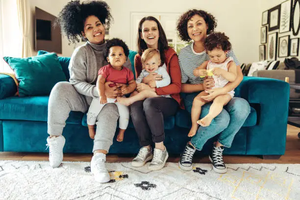 Multi-ethnic mommies sitting with children. Young mothers with babies sitting on sofa and looking at camera.
