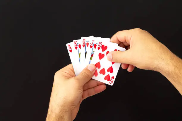 Male hands holding combination of royal flush poker cards on dark background. Casino, luck and fortune concept