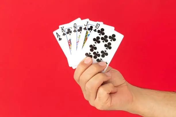 Male hand holding combination of royal flush poker cards on red background. Casino luck fortune concept