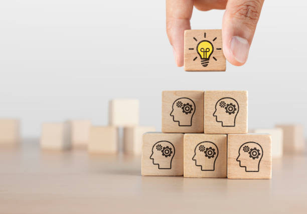 istock Brainstorming, creative idea or innovative idea concept. Wooden blocks with gear head icon arranged in pyramid stair shape and a man is holding the top one with light bulb icon. 1297036691