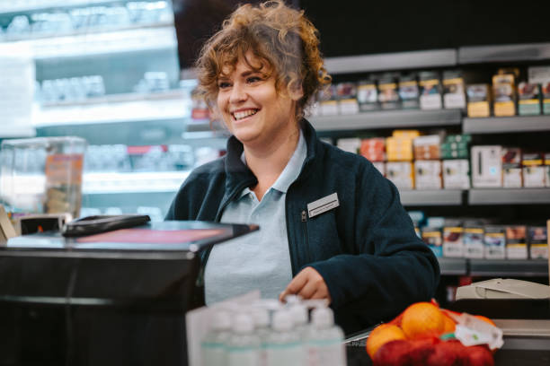 Happy cashier at supermarket checkout Woman working as a cashier in a supermarket. She is smiling at the customer. cashier photos stock pictures, royalty-free photos & images
