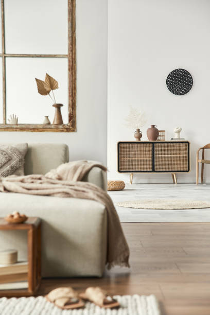 istock Stylish composition of living room with design beige sofa, wooden stool, commode, book, decoration, furniture, window and elegant personal accessories. Modern home decor. Open space. Template. 1297039283