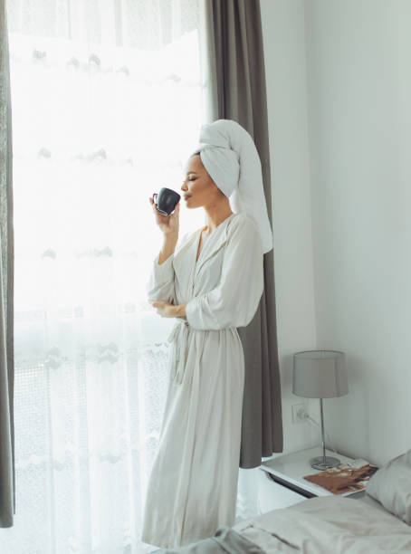 istock Young woman in bathrobe drinking coffee and looking through the window. 1297039324
