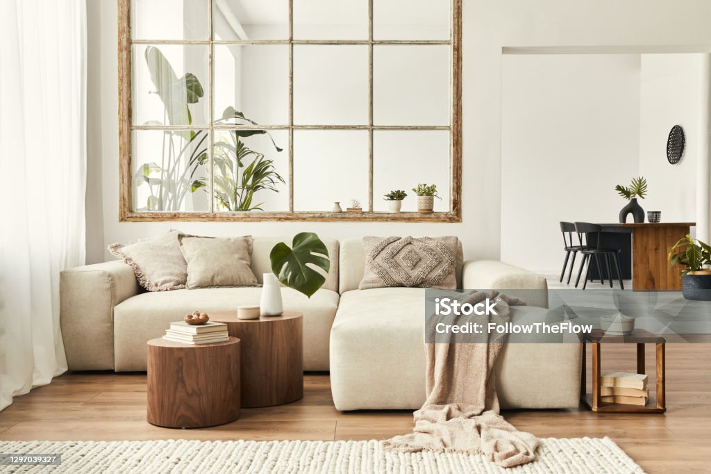 Modern interior of open space with design modular sofa, furniture, wooden coffee tables, plaid, pillows, tropical plants and elegant personal accessories in stylish home decor. Neutral living room. Modern interior of open space with design modular sofa, furniture and elegant personal accessories in stylish home decor. Neutral living room. Living Room Stock Photo