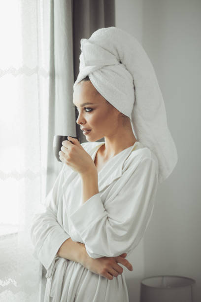 istock Young woman in bathrobe drinking coffee and looking through the window. 1297039344