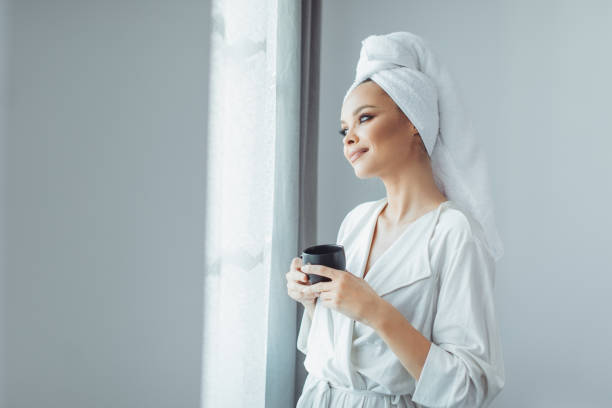 istock Young woman in bathrobe drinking coffee and looking through the window. 1297039510