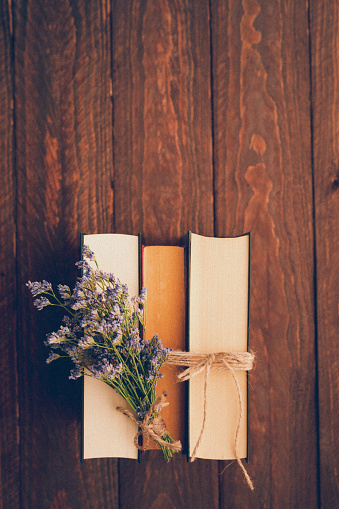 Top view of a beautiful flat lay in retro style with laced old vintage books in a row and a little lilac flower bouquet on dark wooden background and copy space on the top. Useful for wisdom, curiosity, philosophy, love, joyful and best for your soul concepts. Retro editing with added grain. Part of a series.