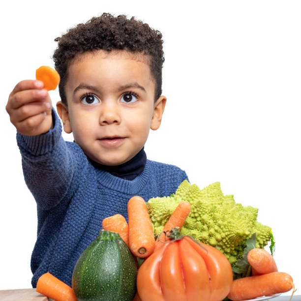 carino ragazzo afro americano che mostra pezzo di verdura a tavola - food healthy eating carrot table foto e immagini stock