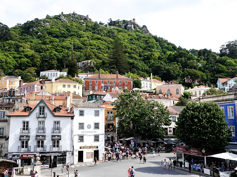 Sintra,Lisbon, Portugal- June 2, 2019: Busy town square Sintra, Portugal. Many people are shopping and eating. Moorish fort wall can be seen high on the hill behind.