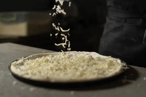 Grated hard cheese lays on the pizza. The process of cooking in production in a pizzeria. Restaurant cooking concept.