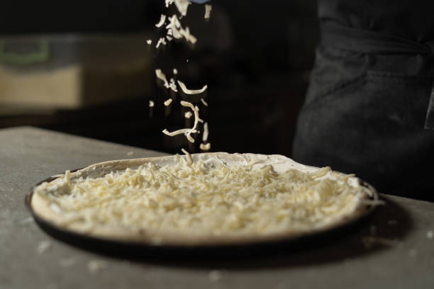 grated hard cheese lays on the pizza. the process of cooking in production in a pizzeria. - mozzarella imagens e fotografias de stock