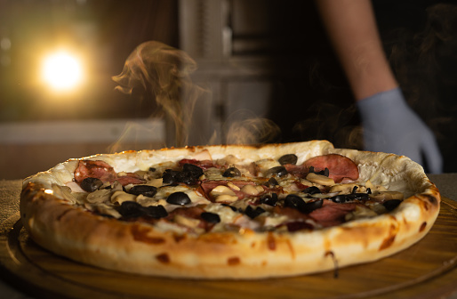 Fresh hot Italian pizza with cheese and steam on the table in a pizzeria. Food delivery. Close-up.