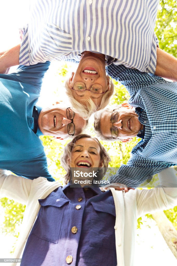 Faces of happy seniors Low angle view shot of four happy seniors embracing outside and laughing at camera. Senior Adult Stock Photo