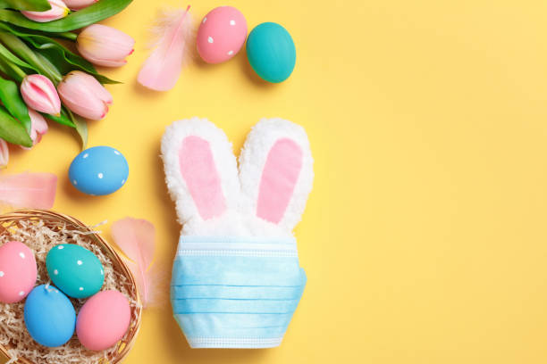 istock Easter concept. Rabbit in a protective medical mask and a basket with colored eggs on a yellow background. 1297053036