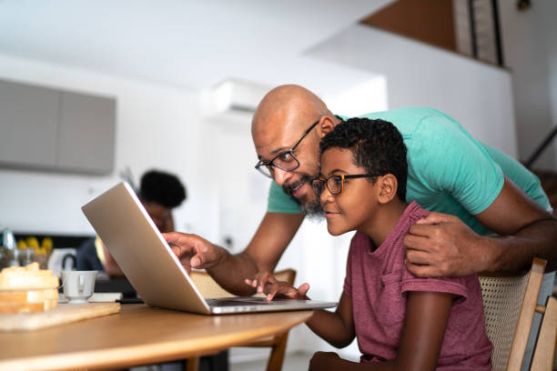 padre che incoraggia il figlio a scuola o a fare una videochiamata / guardare un film - computer child family laptop foto e immagini stock