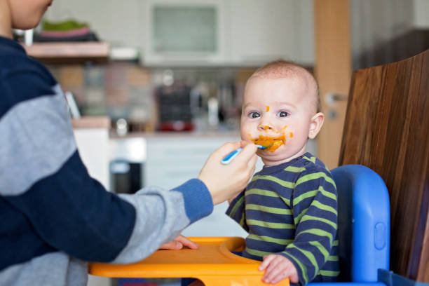 Cute preschool boy, feeding his baby brother with mashed vegetables, baby eating mashed food Cute preschool boy, feeding his baby brother with mashed vegetables, baby eating mashed food for the first time baby food stock pictures, royalty-free photos & images
