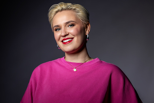 Portrait of attractive young woman looking happy. Pretty caucasian woman with short blond hair against grey background.