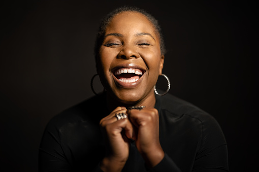 Happy african american woman laughing on against dark background. Cheerful mid adult female in studio.