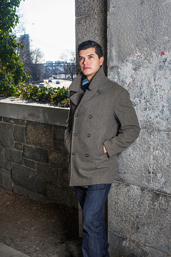 A young guy, hands putting in pockets and standing by a window frame, is deeply thinking