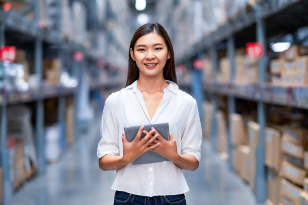 verticale de travailleur asiatique d’entrepôt vérifiant dans le grand centre de distribution d’entrepôt avec la tablette numérique. dans les étagères de fond avec des marchandises. - data center computer programmer women photos et images de collection