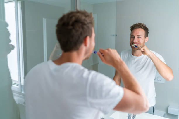 istock Man getting ready in the morning doing hygiene routine brushing his teeth looking in mirror of home bathroom using toothbrush in for clean dental oral care 1297077743