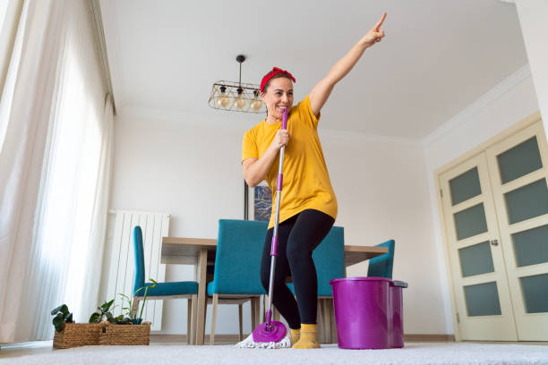 young dreamer woman who suddenly starts singing using the mop in her hand as a microphone while cleaning the floor - spring cleaning women cleaning dancing imagens e fotografias de stock