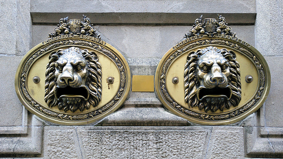 Post Office bronze mailboxes in the shape of the head of two lions, stone wall. Seen in the street in Pontevedra city, Galicia, Spain