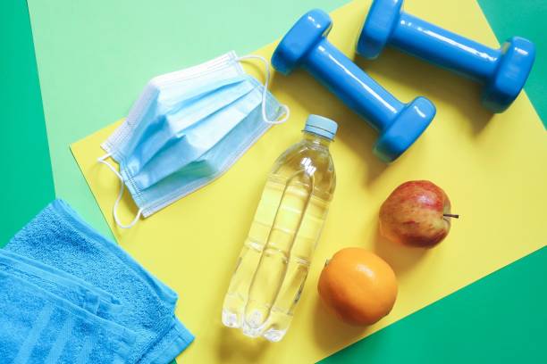 istock Recovery from coronavirus COVID-19. Physical activity, proper nutrition and drinking clean water. Top view photography disposable face mask, water bottle dumbbells, fruits and towel 1297078970