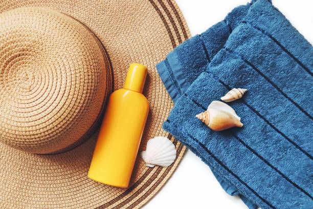 istock Top view flat lay composition summer beauty photography. Wicker sun hat, moisturizing sunscreen lotion, blue cotton towel and seashells 1297080240