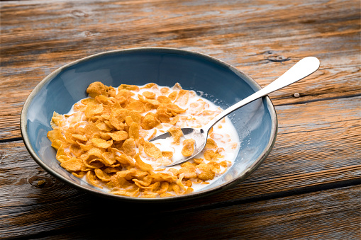Bowl of corn flakes with spoon on wooden table