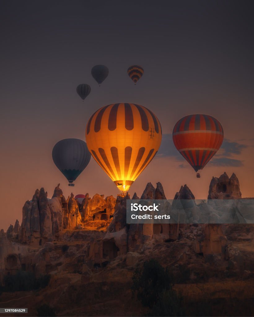 Hot Air balloons flying over rock formations at sunrise in Cappadocia, Goreme, Turkey Spectacular sunset landscape view of hot air balloon illuminated with fire in sky tour over amazing fairy chimneys rock forms on valleys and fields in early morning in Kapadokya, Göreme National Park, Turkiye. Dreamy nature background. Hot Air Balloon Stock Photo