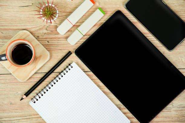 A notebook, paper, pen, calculator and other other personal finance tools are seen scattered on a desk in this at home finance concept.