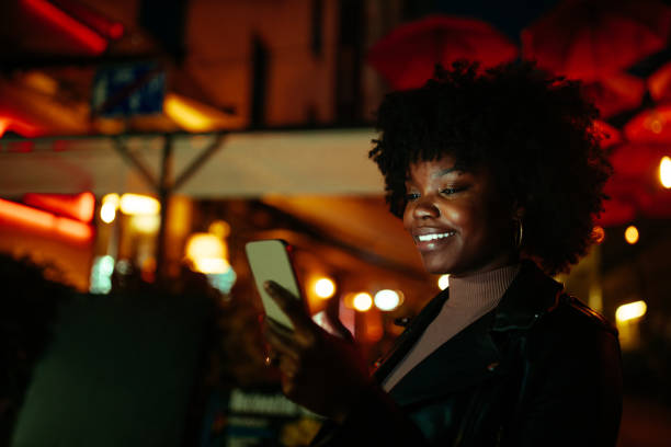 istock Smiling afro female outdoors at night, checking social media 1297090373