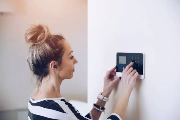 Blonde woman entering code on home security alarm keypad. Alarm code.