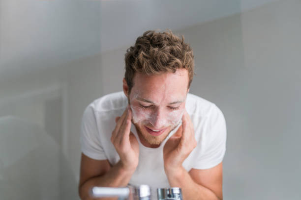 mens die gezicht met gezichtsreinichtreeker waszeep in badkamersgootsteen thuis was - gezicht wassen stockfoto's en -beelden