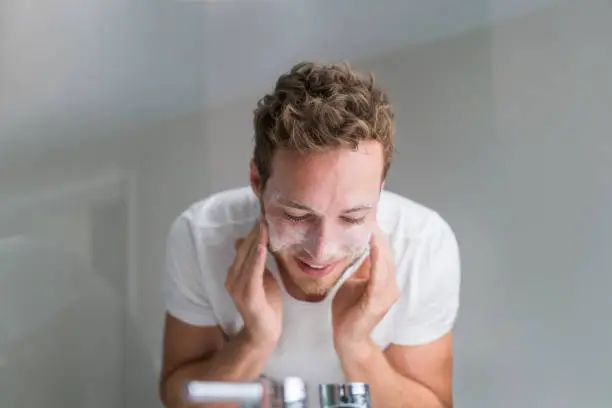 Photo of Man washing face with facial cleanser face wash soap in bathroom sink at home