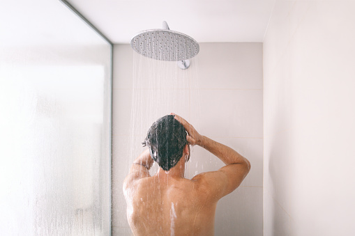 Hombre tomando una ducha lavando el cabello con champú producto bajo el agua que cae de la cabeza de la ducha de lluvia de lujo. Mañana rutina de lujo hotel estilo de vida chico ducharse. higiene del cuidado del cuerpo photo