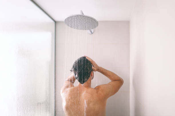 Man taking a shower washing hair with shampoo product under water falling from luxury rain shower head. Morning routine luxury hotel lifestyle guy showering. body care hygiene stock photo