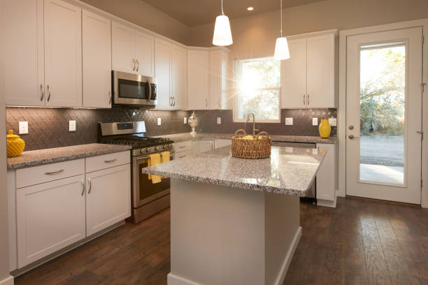 istock Modern Light and Bright Kitchen with Island, Dark Wood Floors, Grey Countertops, with White Cabinets and Sunflare Coming in Through Window 1297094947