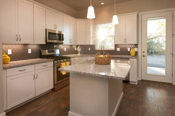 Modern Light and Bright Kitchen with Island, Dark Wood Floors, Grey Countertops, with White Cabinets and Sunflare Coming in Through Window stock photo