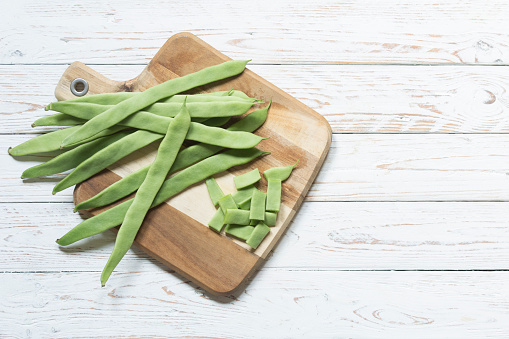 A Green beans on a cutting board and on a rustic white wood background. copy for space and text