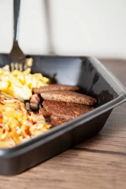 Eggs, breakfast sausage, and cheesy hash browns in a black take out container