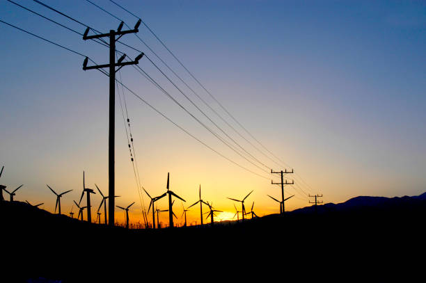 Windmill farm in the desert at sunset in Palm Springs, California with power lines going to the city. stock photo